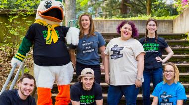 Students with the duck mascot outside sitting on steps